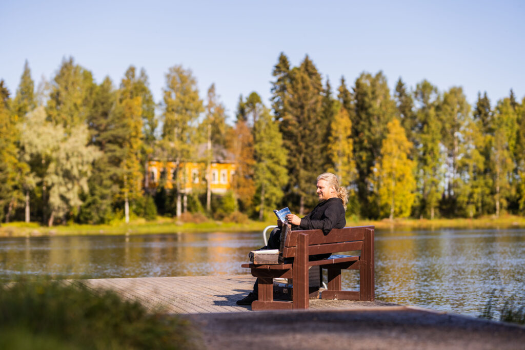 Mies istumassa ja lukemassa Kalevalaa laiturilla